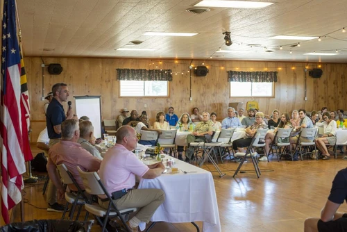 A man with a microphone talks with people sitting at tables.