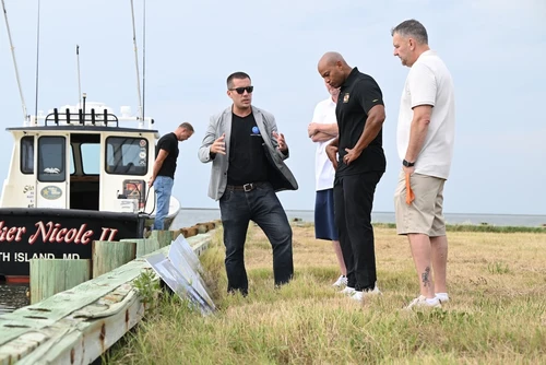 A group of people talk near a boat.