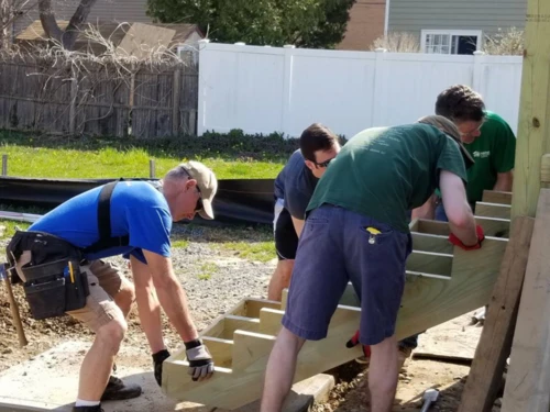 Volunteers lifting and installing a wooden staircase on a home construction site.
