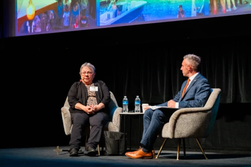 Mary Means and Secretary Jake Day sit in armchairs on a stage, engaged in a discussion during a presentation.