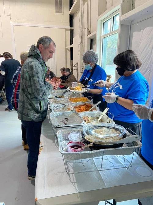 Volunteers in blue shirts serve meals to community members at a food pantry.