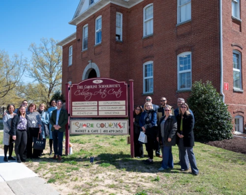 A group shot of people standing next to a sign for "The Caroline Schoolhouses".