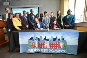 A group of people standing behind a sign saying "Reinvest Baltimore".