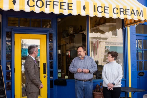 Three people talk in front of a restaurant.