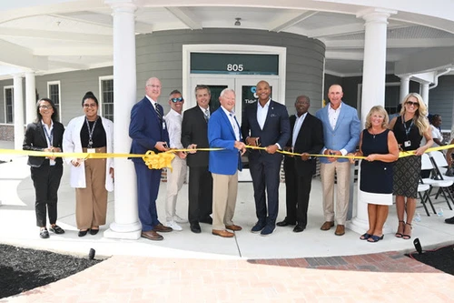 A group of people cutting a large yellow ribbon.