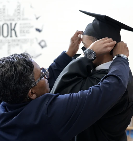 DJS staff assisting a young person with their cap and gown regalia. The young person completed their high school requirements to earn their diploma at the Juvenile Services Educational Program (JSEP).