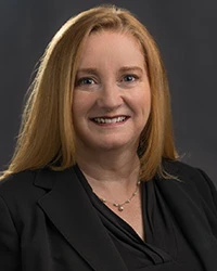Woman with long blond hair wearing a necklace, black blazer and blouse smiling at camera