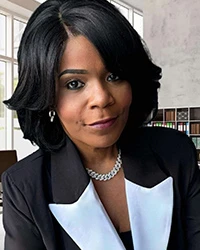 Woman with side-parted black hair wearing a necklace and black-and-white blazer facing the camera