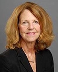 Woman with reddish hair wearing a black blazer and necklace and smiling at camera