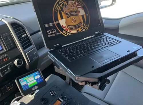 A Crew Cab pickup truck console showing a laptop, radio mount, cup holders, USB/12V charger, and lockbox.