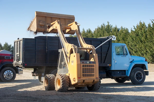 Manure being loaded into a truck with a blue cab for transport