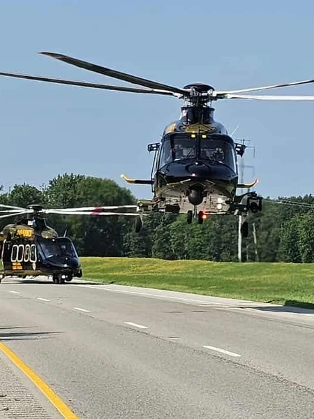 A Maryland State Police helicopter flying low over a road with another landed helicopter