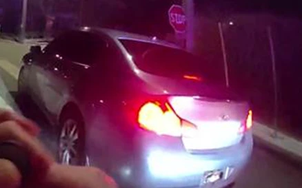 A silver car is stopped at night with glowing red taillights and a visible license plate.