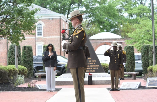 A uniformed officer holding a red rose stands solemnly in a memorial area. 
