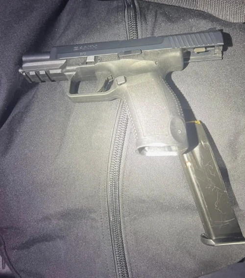 A black handgun with a detached magazine lies on a dark fabric surface with a visible zipper.