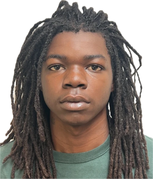 A person with long dreadlocks and a neutral expression is wearing a green shirt against a plain black background. 
