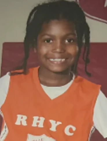 A young boy wearing a white long sleeve shirt and a orange basketball jersey smiling