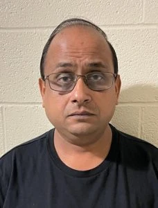 a man wearing a black shirt wearing glasses standing in front of a cylinder wall. 