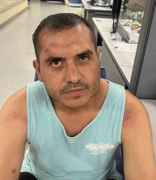 A hispanic man wearing a light blue tank top with a moustache and short black hair. 
