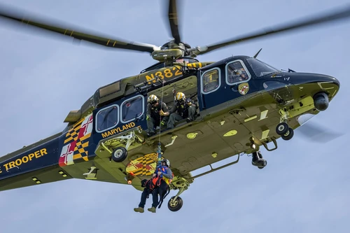 A Maryland State Police Helicopter conducts a hoist exercise with a black Labrador K-9. 