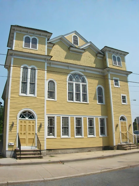 A symmetrical two-story yellow building with white trim, arched windows, and two prominent towers.
