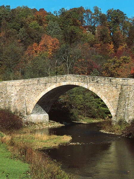 Stone arch bridge spanning a river, framed by trees with fall foliage.