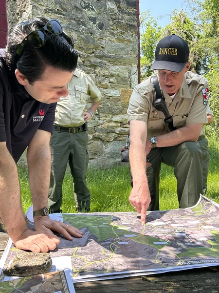 A park ranger and consultants review a large map together during an outdoor site visit.