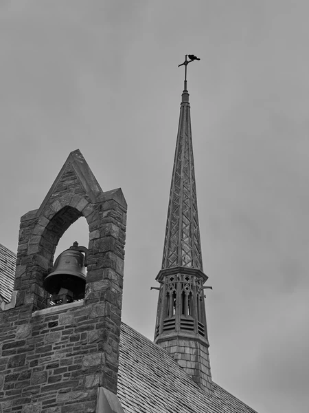 Stone church bell tower and steeple against an overcast sky.