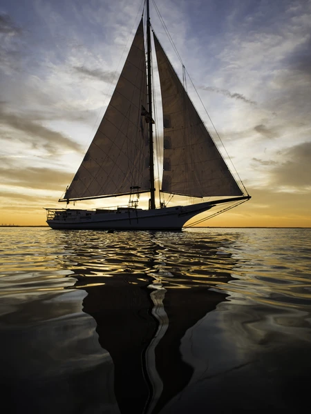 A sailboat, the Wilma Lee, silhouetted against a sunset with reflective water and colorful sky.