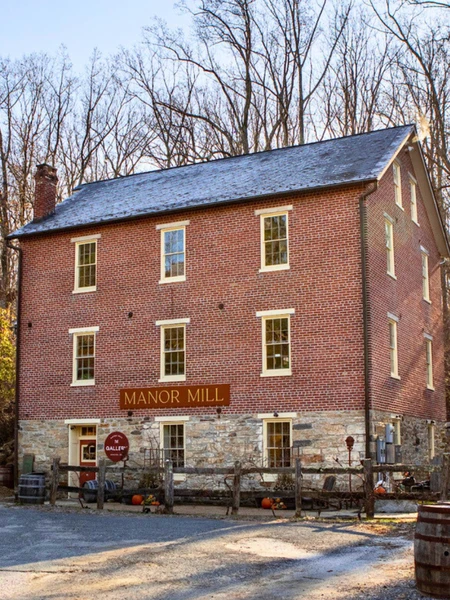 Red brick and stone building surrounded by trees on a sunny and clear day. Sign on the building reads "Manor Mill."