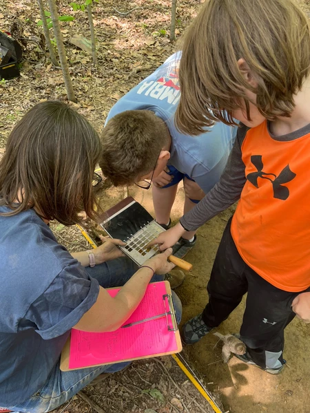 An adult and two children examine a soil color chart at an outdoor excavation site.