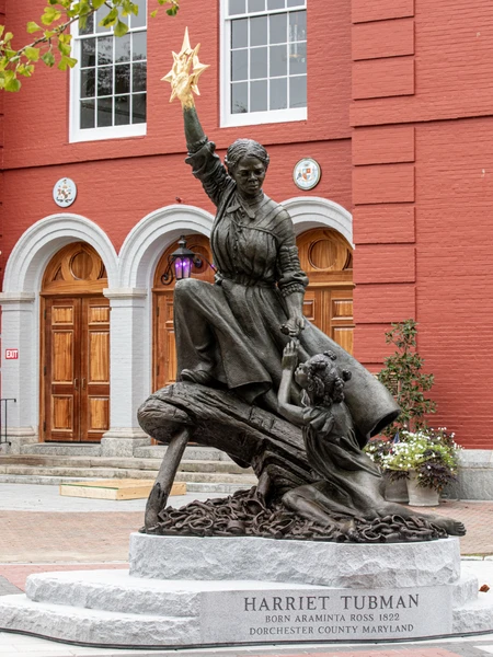 Bronze statue of Harriet Tubman holding a golden star, located in front of a red brick building.
