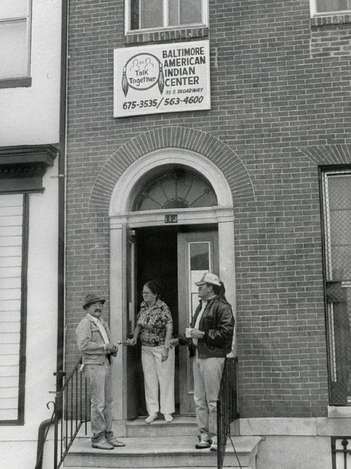 Three men standing on the stoop of a building, sign reading Baltimore American Indian Center