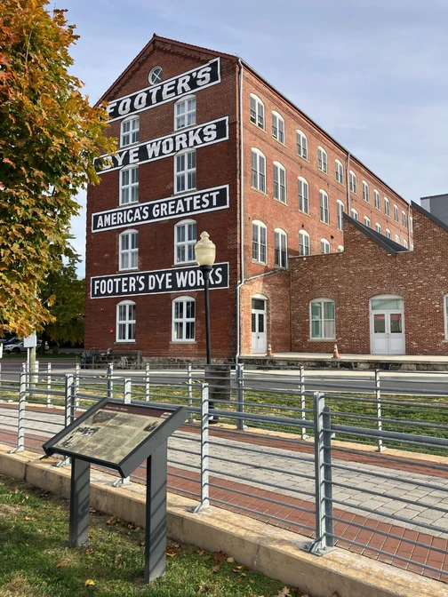 The brick Footer's Dye Works building with large white lettering and a historical marker in the foreground.