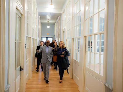 A group of people walking down a well-lit hallway with glass-paneled doors at PS 103.
