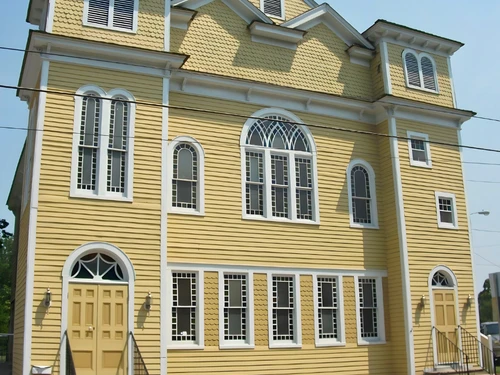 A symmetrical two-story yellow building with white trim, arched windows, and two prominent towers.