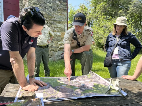 A park ranger and consultants review a large map together during an outdoor site visit.