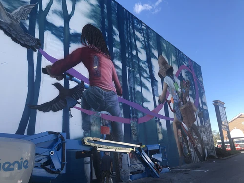 Mural of two people on bicycles surrounded by trees and birds.