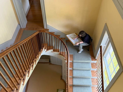Overhead view of a staircase and person sketching in a hallway.