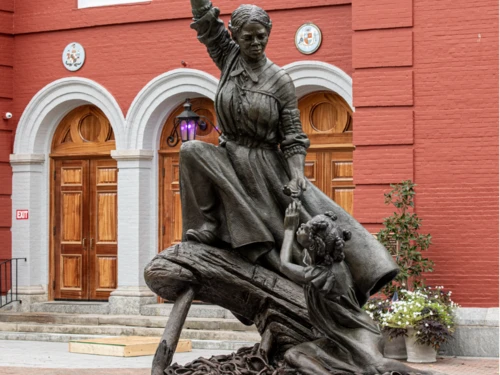 Bronze statue of Harriet Tubman holding a golden star high while reaching down to guide a child over a pile of broken shackles.