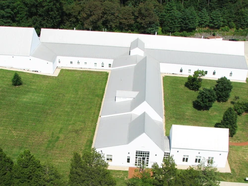 Aerial view of a white building complex with gray roofs, surrounded by green lawns and trees.