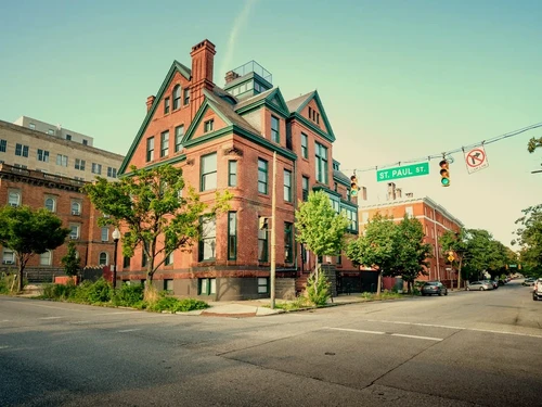 Ornate red brick Queen Anne style house with green trim on St. Paul Street, featuring gables and a rooftop deck.
