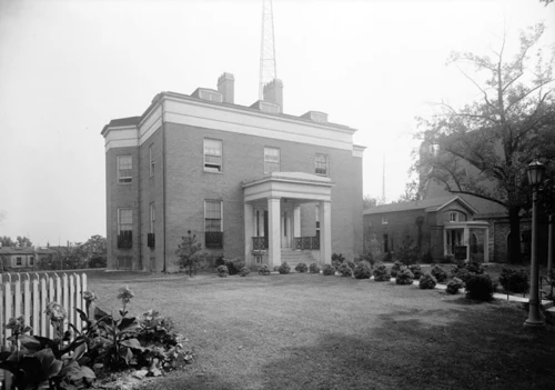 Brick building with columns and antenna, surrounded by a lawn and trees.