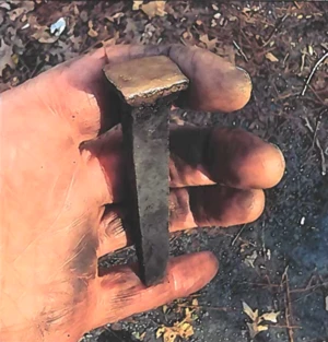 Large, square brass spike held in a person's hand.