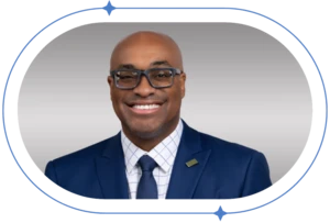 African American man in blue suit smiling in front of blurred background.