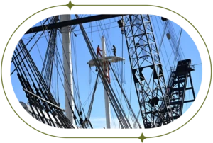 Two people stand on a deck among ship rigging next to a crane.