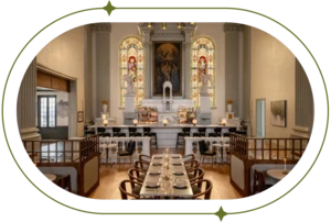 Historic chapel with stained glass windows, set up with restaurant style tables in front.
