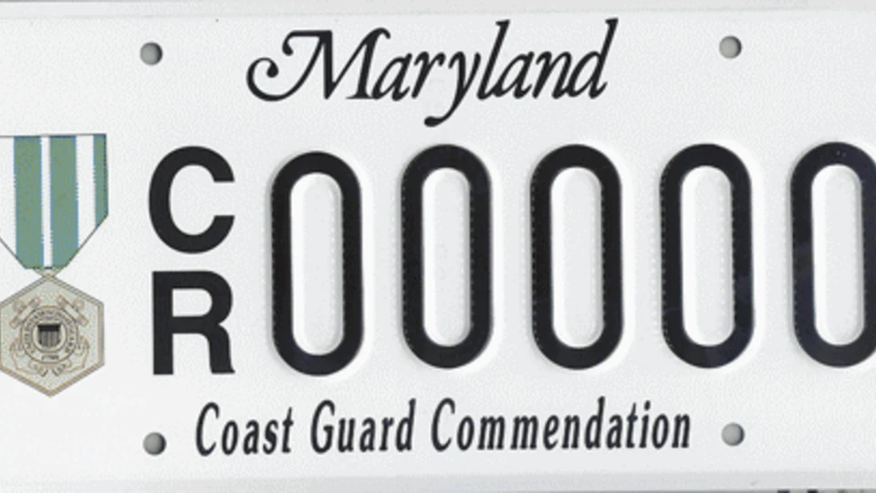 White license plate with the Coast Guard Commendation medal to the left of the plate number.
