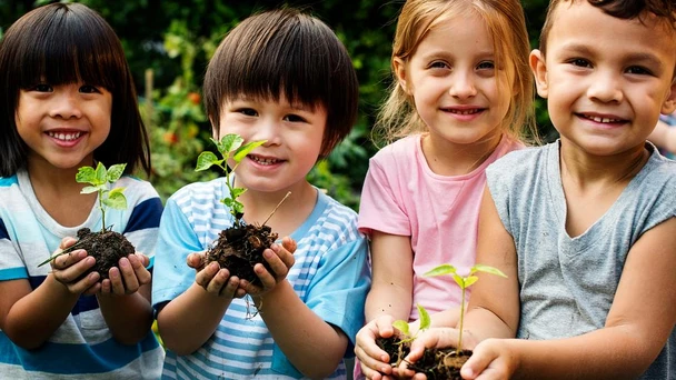 kids stand together holding plants in dirt
