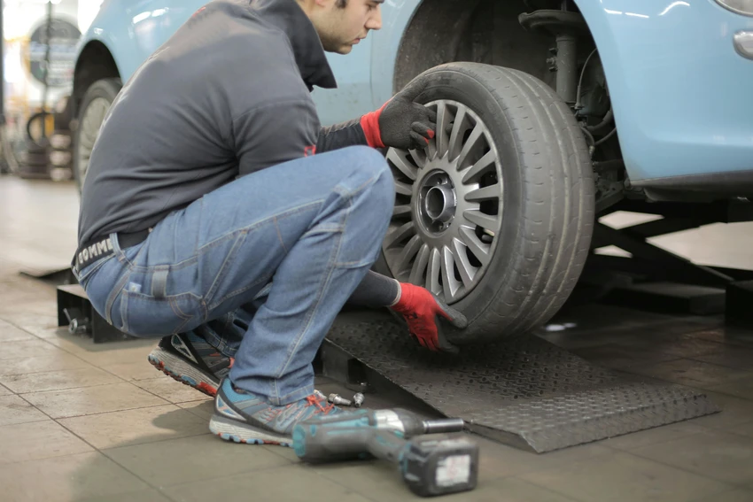 a person squats next to a car to change the tire